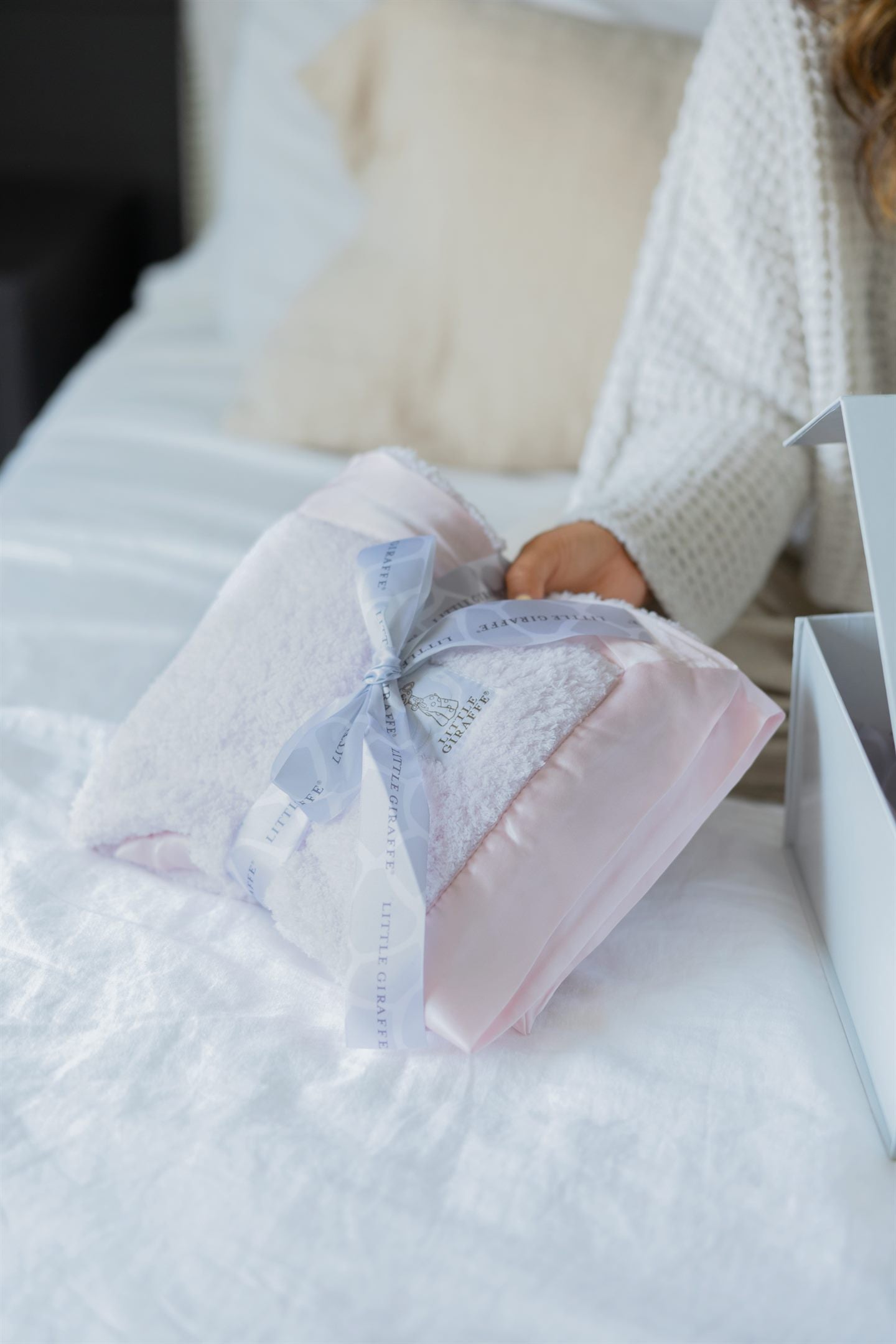 Pink Little Giraffe blanket with a ribbon, being unwrapped as a gift