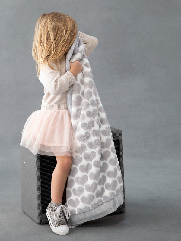 A child holding a toddler blanket with hearts on it