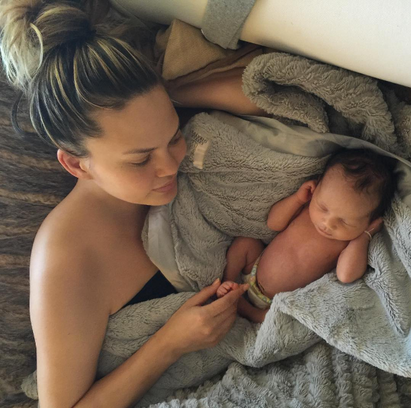 Chrissy Teigen and baby laying in gray baby blanket