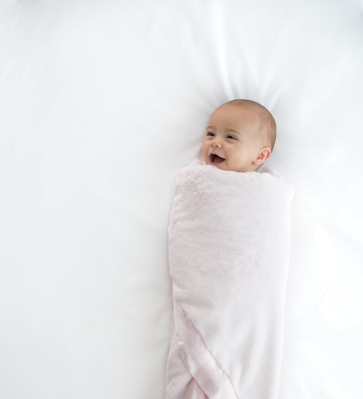Baby smiling wrapped in pink baby blanket