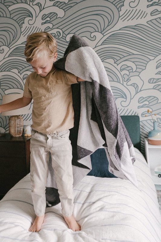 Toddler standing on bed with big kid blanket
