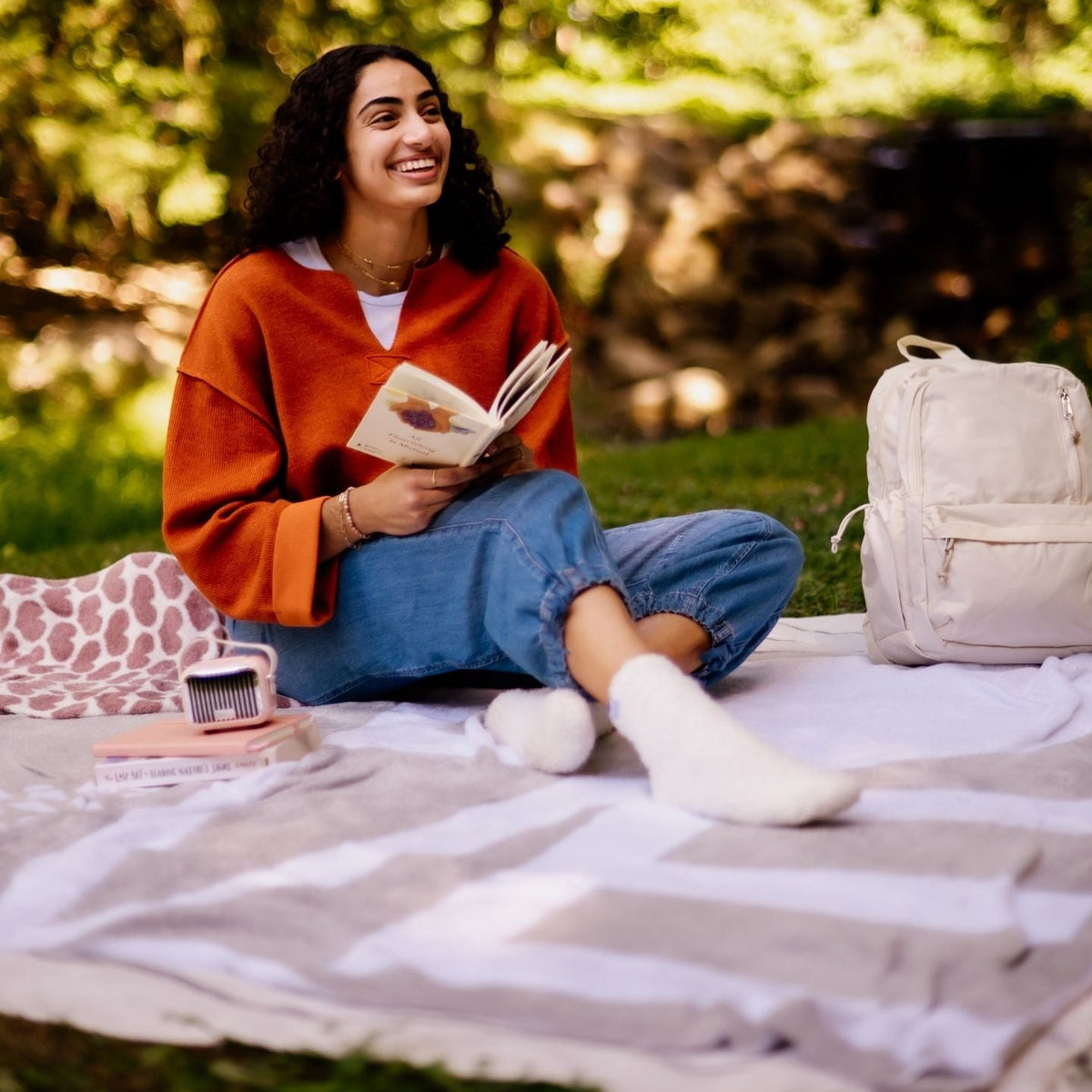 Woman sitting on a blankets in a park, reading a book