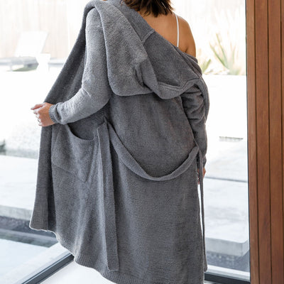 Person wearing a gray robe standing by a window